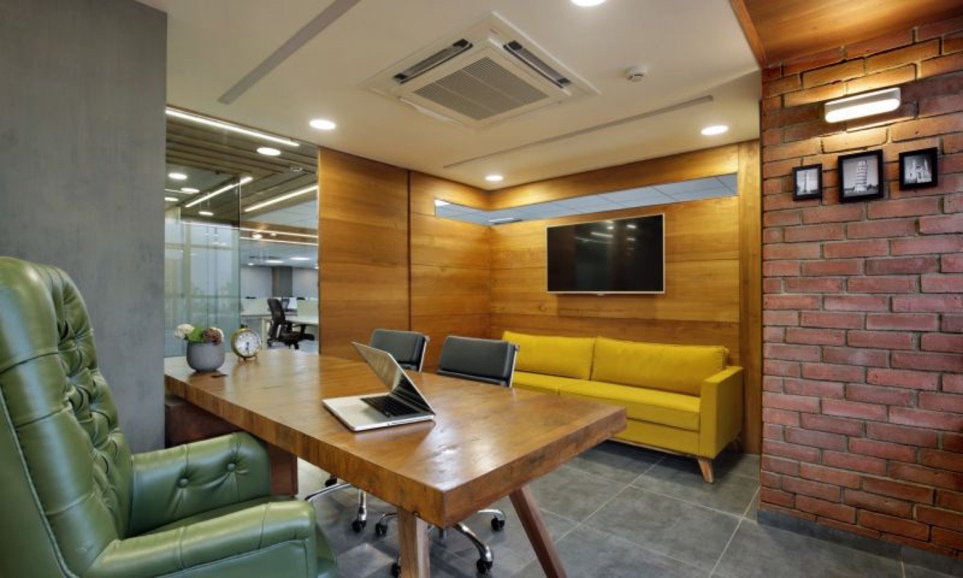 A meeting room with a yellow sofa, timber table and exposed brick